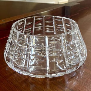 K&ouml;nnte beinhalten: Eine klare, geschliffene Kristallschale mit einer breiten, ausgestellten Form. Die Schale weist komplizierte geometrische Muster und Sternmuster auf, die das Licht reflektieren. Die Schale ist wahrscheinlich aus Bleikristall und f&uuml;r dekorative Zwecke geeignet.