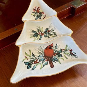 Può includere: Un piatto da portata in ceramica bianca a forma di albero di Natale con tre sezioni. Il piatto è decorato con un cardinale, agrifoglio e bacche.