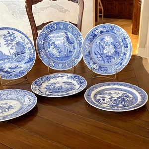 Op de afbeelding: Een verzameling van zes blauw-witte decoratieve borden. De borden tonen diverse landschappelijke en bloemmotieven. Ze zijn op een donkere houten tafel geplaatst, wat hun gedetailleerde patronen en klassieke stijl benadrukt. Een klassieke toevoeging aan elk interieur.