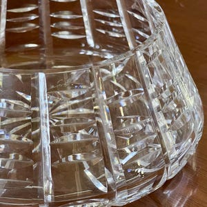 K&ouml;nnte beinhalten: Eine transparente, geschliffene Kristallschale mit breiter, ausgestellter Form. Die Schale weist vertikale und abgewinkelte Schliffmuster auf, die eine strukturierte Oberfl&auml;che erzeugen. Die Schale ist so konzipiert, dass sie Licht reflektiert. Geeignet zum Servieren oder Dekorieren.