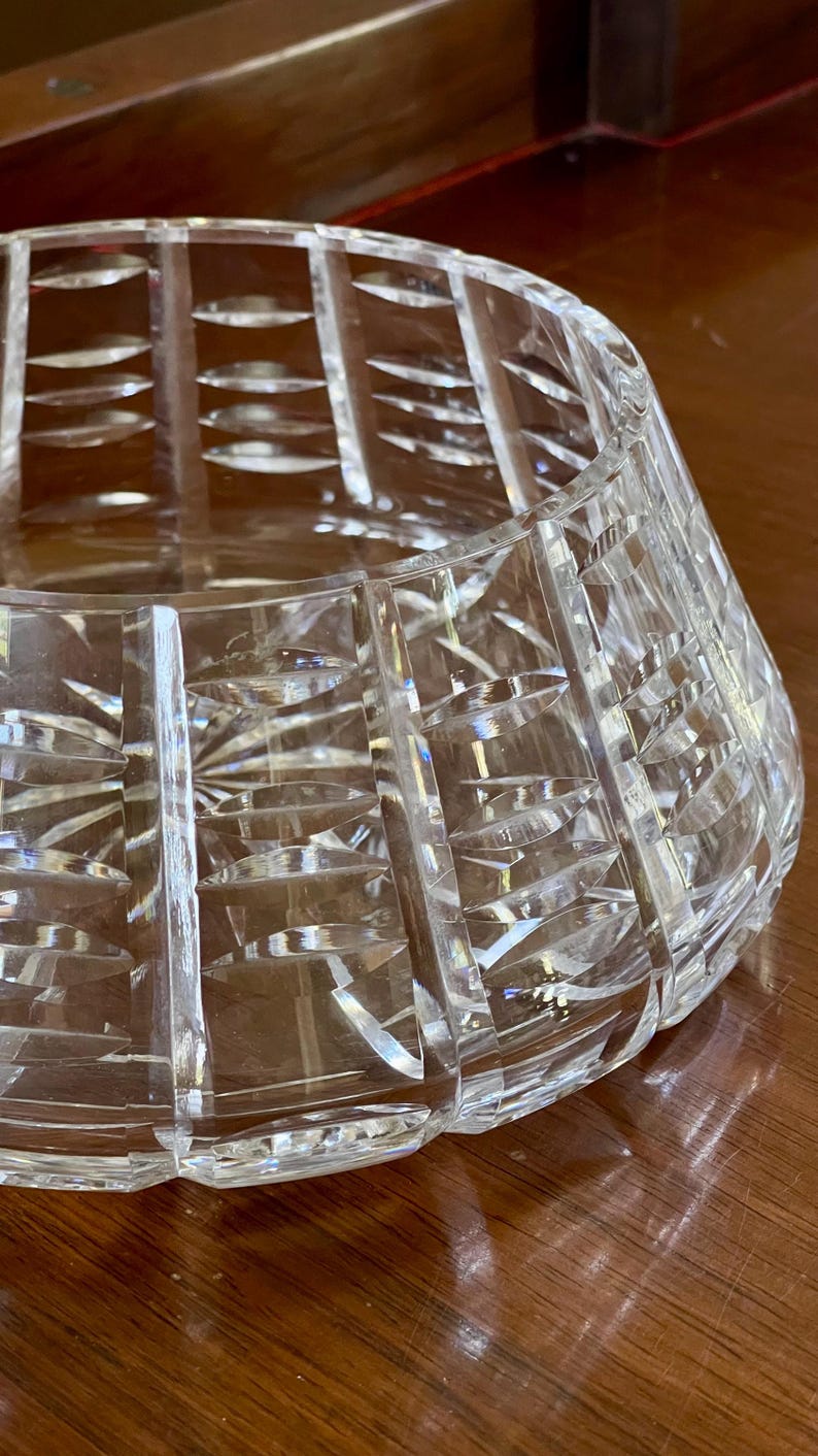 K&ouml;nnte beinhalten: Eine transparente, geschliffene Kristallschale mit breiter, ausgestellter Form. Die Schale weist vertikale und abgewinkelte Schliffmuster auf, die eine strukturierte Oberfl&auml;che erzeugen. Die Schale ist so konzipiert, dass sie Licht reflektiert. Geeignet zum Servieren oder Dekorieren.