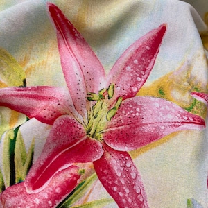 May include: A close-up of a pink lily flower with white spots on the petals. The flower is on a light yellow background with a subtle floral pattern.