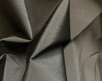 Puede incluir: Primer plano de una tela negra con una textura suave y sedosa. La tela está doblada y drapeada, creando un aspecto suave y fluido.
