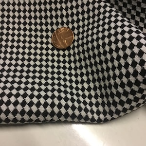 Op de afbeelding: Zwart-wit geblokt stof met een kleine munt erop. De stof heeft een geweven textuur.