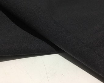 Puede incluir: Primer plano de una tela negra con una superficie lisa y ligeramente texturizada. La tela está doblada por la mitad, creando un pliegue en el centro.
