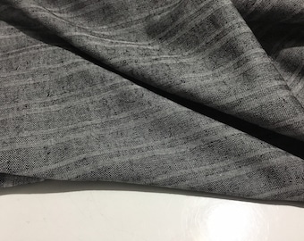Könnte beinhalten: Nahaufnahme eines grauen und weißen gestreiften Stoffes mit Fischgrätenbindung. Der Stoff ist gefaltet und drapiert, wodurch die Textur und das Muster sichtbar werden.