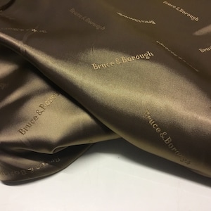 May include: Close-up of a brown satin fabric with the text "Bruce & Borough" embossed in gold.