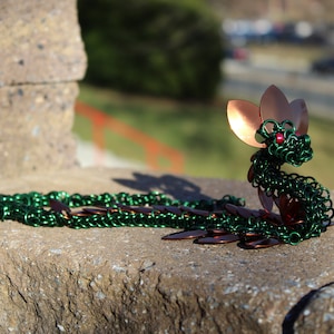 Peut inclure: Sculpture de dragon en maille de chaîne de couleur verte et cuivre. Le dragon a une aile en cuivre et un œil en perle rouge.