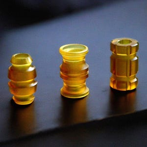 May include: Three amber-coloured, cylindrical objects with a segmented design. The objects are arranged in a row, each with a slightly different shape and size. The background is a dark, solid colour.
