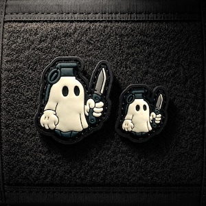 May include: Two rubberised morale patches featuring a cartoon ghost character with a grenade-shaped head, holding a small knife in one hand. The ghost is off-white with dark grey accents and a black border, set against a black textured background.