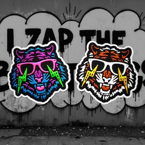 May include: Two tiger head stickers with sunglasses and lightning bolt designs. One tiger is blue and purple with pink glasses and green lightning bolts. The other is orange and white with white glasses and yellow lightning bolts. The background is a graffiti wall with the words "I ZAP THE BUGS".