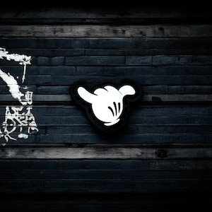 Könnte beinhalten: Eine weiße Handgeste, die an eine dunkle Holzwand gemalt ist. Die Hand macht das Shaka-Zeichen, eine beliebte hawaiianische Geste für Frieden, Glück und Aloha.