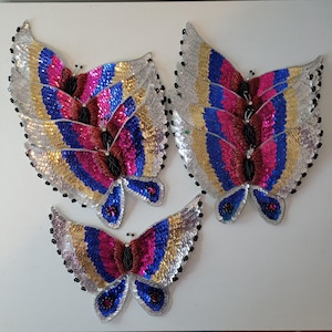 May include: Four sequined butterfly appliques in various sizes. The butterflies are made of silver, blue, pink, and red sequins. They are perfect for adding a touch of sparkle to any project.