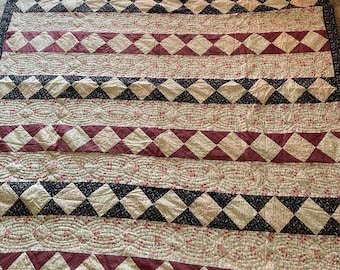 May include: A quilt with a patchwork design featuring alternating rows of burgundy and white diamond patterns, black and white diamond patterns, and a floral print fabric. The quilt is quilted with a wavy pattern.