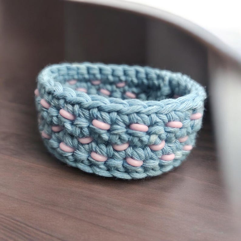 Puede incluir: Un anillo de crochet azul claro con cuentas rosas tejidas en el dise&ntilde;o.