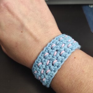 Puede incluir: Un brazalete de crochet azul claro con cuentas rosas tejidas en el dise&ntilde;o.