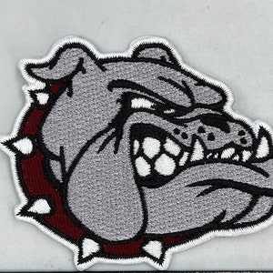 May include: A gray embroidered bulldog head patch with a maroon and white spiked collar. The bulldog has a fierce expression with a bared mouth and sharp teeth.