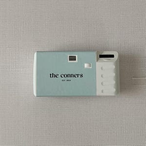 May include: A light blue disposable camera with the text "the connors est 2024" printed on the front.