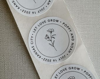 Puede incluir: Pegatina redonda blanca con texto negro y un dibujo simple de una flor. El texto dice "Let love grow. Poppy and Noah. July 16, 2022. Kansas City."