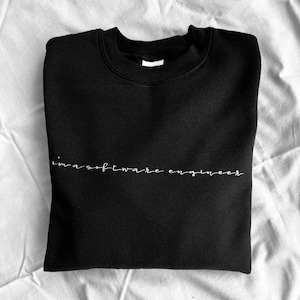 Könnte beinhalten: Schwarzer Pullover mit dem Text "i'm a software engineer" in weißer Kursivschrift.