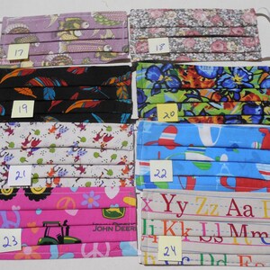 May include: A set of 8 colorful fabric face masks with different patterns. The masks are numbered 17 through 24. The patterns include fish, flowers, feathers, a jungle scene, a children's alphabet, and a tractor.