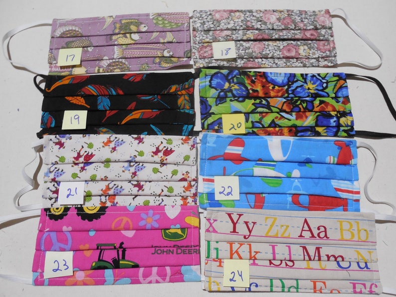 May include: A set of 8 colorful fabric face masks with different patterns. The masks are numbered 17 through 24. The patterns include fish, flowers, feathers, a jungle scene, a children's alphabet, and a tractor.