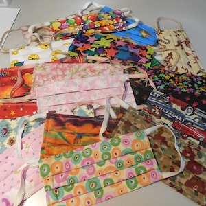 May include: A collection of assorted fabric face masks with elastic ear loops. The masks feature various patterns, including stars, smiley faces, floral prints, and car designs. Colors include red, blue, pink, and green.