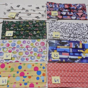 May include: Eight different fabric face masks with various patterns, including musical notes, circles, and American flags. Each mask has a yellow sticky note with a number on it, ranging from 57 to 64.