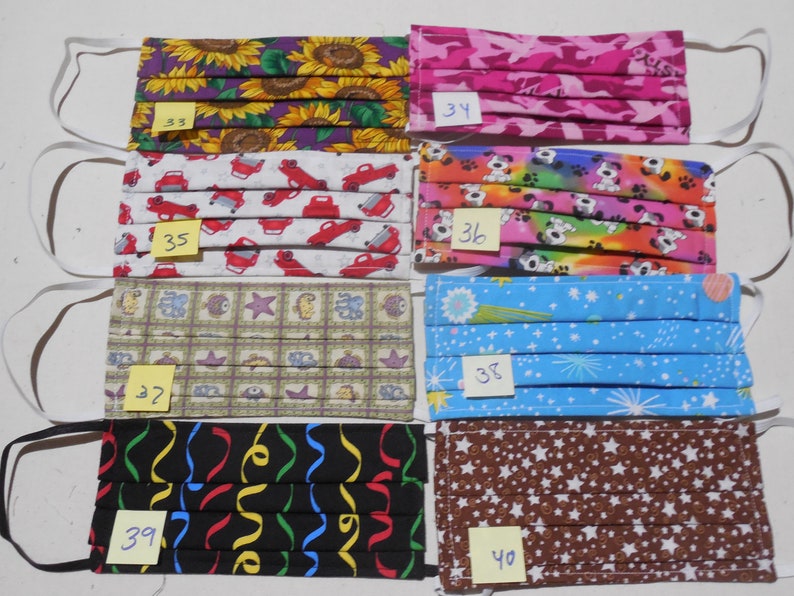 May include: Ten fabric face masks with different patterns, including sunflowers, cars, dogs, stars, and confetti. Each mask has a number written on it, ranging from 33 to 40.