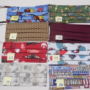 May include: Six different fabric face masks with various patterns. The masks are pleated and have elastic ear loops. The patterns include a blue and red fire truck design, a green and brown animal print, a brown with white polka dots, a maroon solid color, a red with white Star Wars characters, a white with blue trucks, a gray with brown airplanes, and a red, white, and blue patriotic design. The masks are numbered 49 through 56.