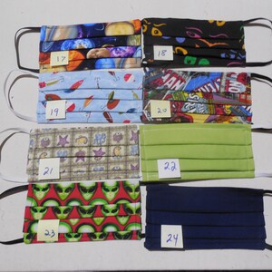 May include: A collection of seven face masks with various patterns and colors. Designs include planets, cartoon eyes, fishing lures, comic book panels, sea creatures, solid green, alien heads, and solid navy blue. Each mask has elastic ear loops.