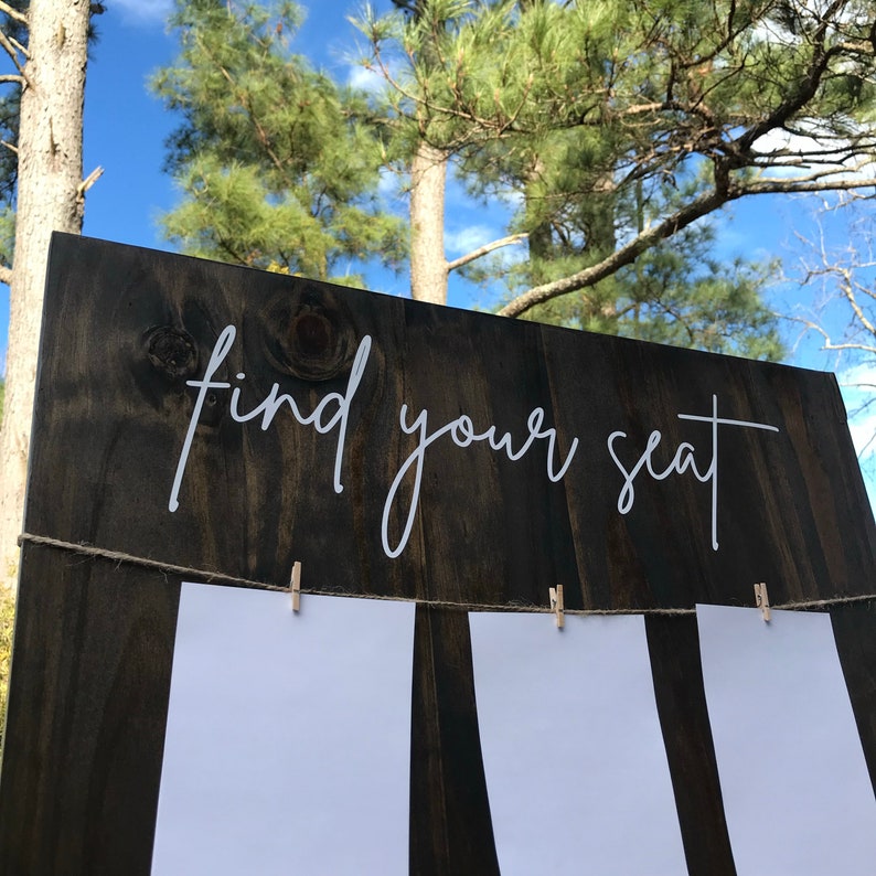 May include: A dark brown wooden sign with the text "find your seat" in white script. The sign has three white cards attached with clothespins.