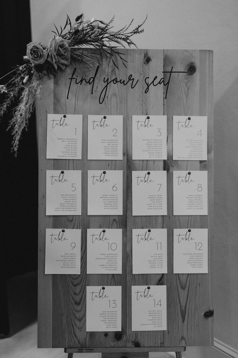 May include: A wooden seating chart with white cards listing table numbers and guest names. The sign reads "find your seat".