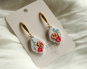 May include: A pair of white teardrop-shaped earrings with gold hooks. The earrings are decorated with pink, red, and white flowers and green leaves.