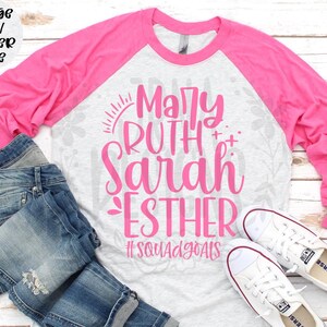 May include: A heather gray and pink raglan shirt with the names Mary, Ruth, Sarah, and Esther in pink script. The shirt is paired with blue denim shorts and white sneakers. The text "#SquadGoals" is also visible.