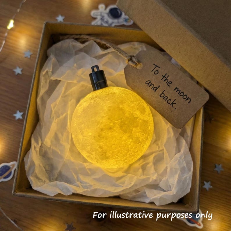 3D printed moon ornament in a kraft paper gift box with tissue paper and handwritten space-themed gift tag, glowing with soft ambient light.