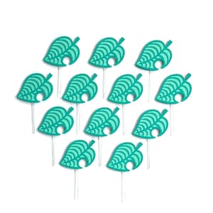 May include: A collection of teal leaf-shaped cupcake toppers. Each topper features a detailed leaf design and is attached to a clear plastic stick. The toppers are arranged on a white background.