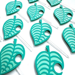 May include: A collection of teal leaf-shaped party picks. Each pick features a detailed leaf design with a clear plastic stem. The leaves are a vibrant teal color, and the design is reminiscent of a popular video game.