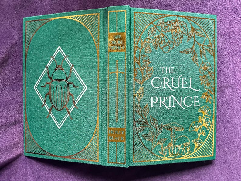 May include: Hardcover book titled "The Cruel Prince" by Holly Black. The book has a teal cover with gold foil accents, including a beetle illustration and floral designs. The spine features a gold sword and the title.