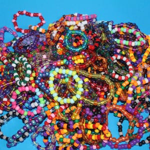 Può includere: Una vivace collezione di braccialetti di perline in vari colori, tra cui rosso, arancione, giallo, verde, blu, viola e nero. I braccialetti sono fatti di piccole perline colorate, su sfondo blu.