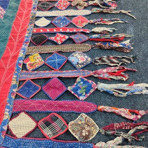May include: A colorful patchwork quilt with a fringe border. The quilt is made of various fabrics in shades of red, blue, green, and white. The fringe is made of strips of fabric in various colors and patterns.