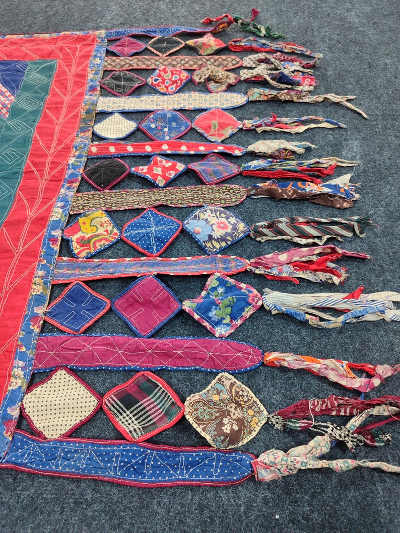 May include: A colorful patchwork quilt with a fringe border. The quilt is made of various fabrics in shades of red, blue, green, and white. The fringe is made of strips of fabric in various colors and patterns.