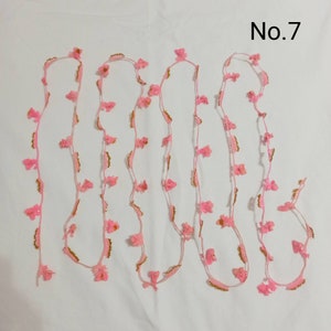 May include: Pink and gold floral trim with a No. 7 label. This trim is made of delicate crocheted flowers and is perfect for adding a touch of elegance to any project.
