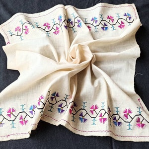 May include: A white cotton fabric square with a decorative embroidered border. The border features a repeating pattern of stylized flowers in shades of pink, blue, and black.