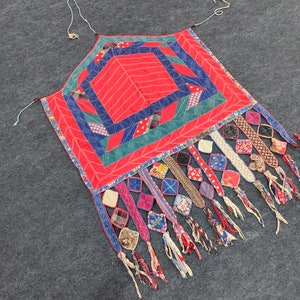 May include: A red, blue, and green patchwork quilt with a geometric design. The quilt has a fringe border with colorful fabric scraps.