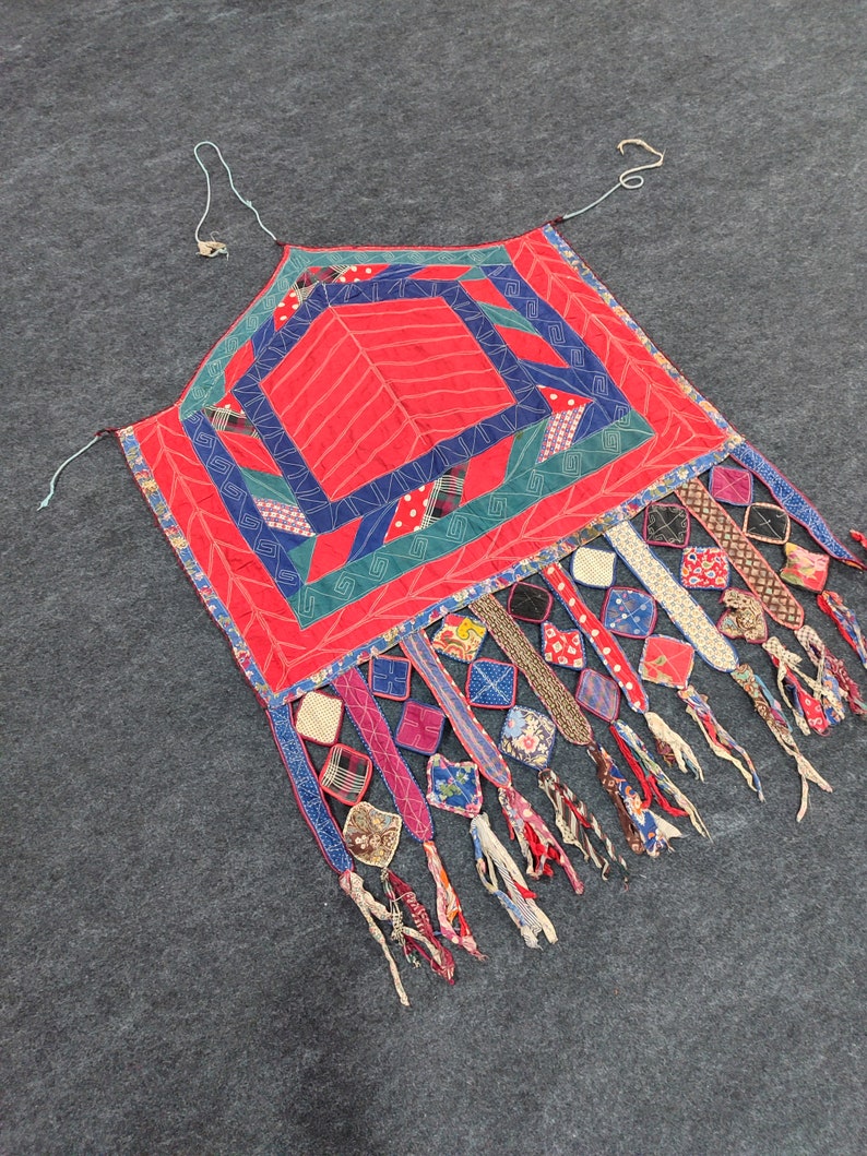 May include: A red, blue, and green patchwork quilt with a geometric design. The quilt has a fringe border with colorful fabric scraps.