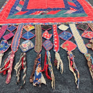 May include: A red, blue, and green patchwork quilt with a fringe of colorful fabric strips. The quilt is made of various fabrics, including cotton and silk. The quilt is a traditional folk art form.