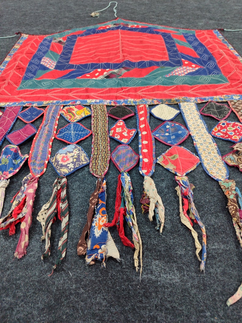 May include: A red, blue, and green patchwork quilt with a fringe of colorful fabric strips. The quilt is made of various fabrics, including cotton and silk. The quilt is a traditional folk art form.