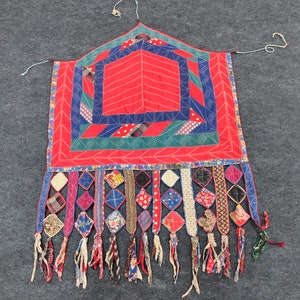 May include: A red, blue, and green patchwork quilt with a geometric design and fringe. The quilt is made of various fabrics and has a unique, handmade look.