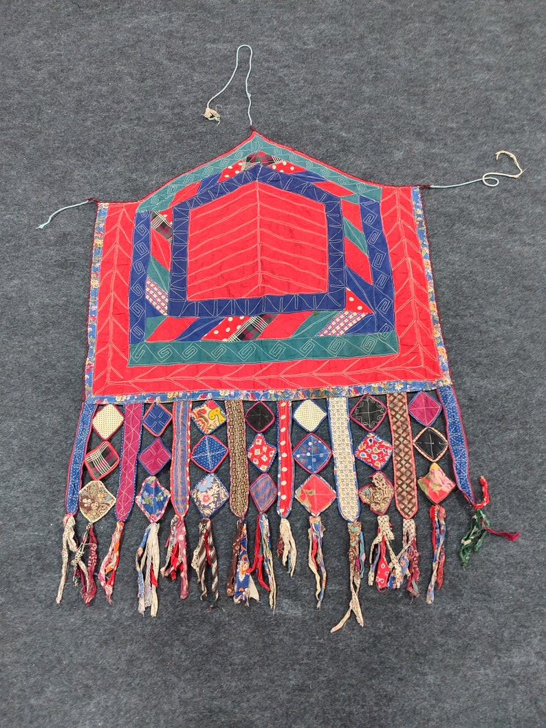 May include: A red, blue, and green patchwork quilt with a geometric design and fringe. The quilt is made of various fabrics and has a unique, handmade look.